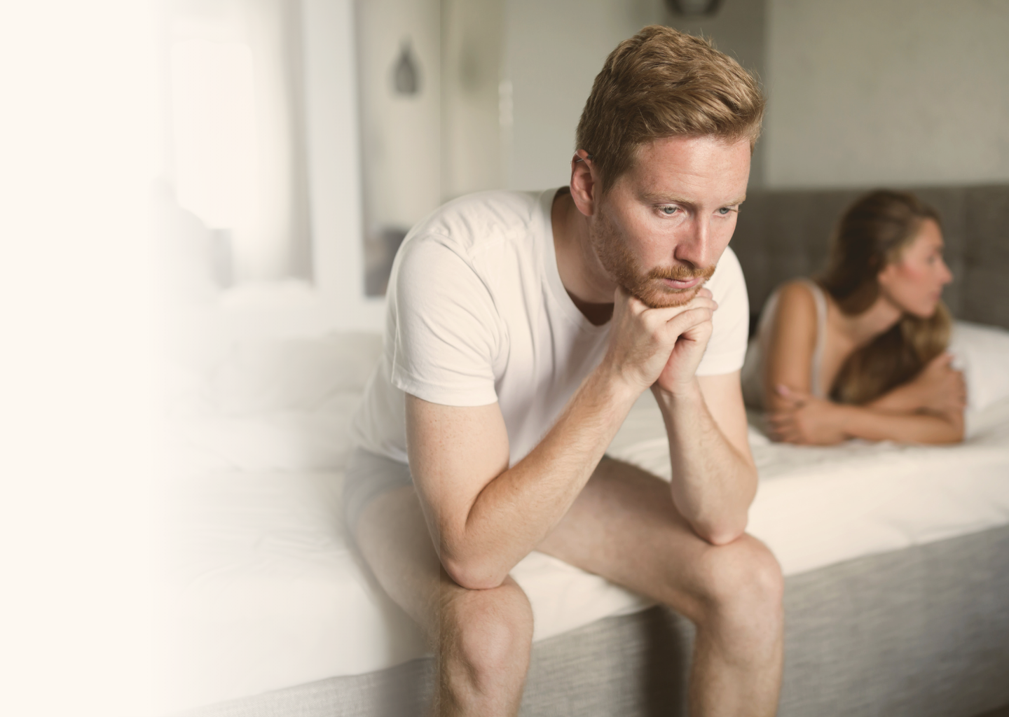 A couple sitting apart on a bed, distant and hurting